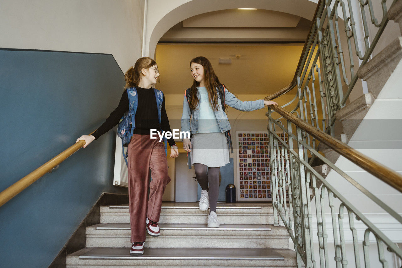 Smiling female friends moving down from staircase in school building