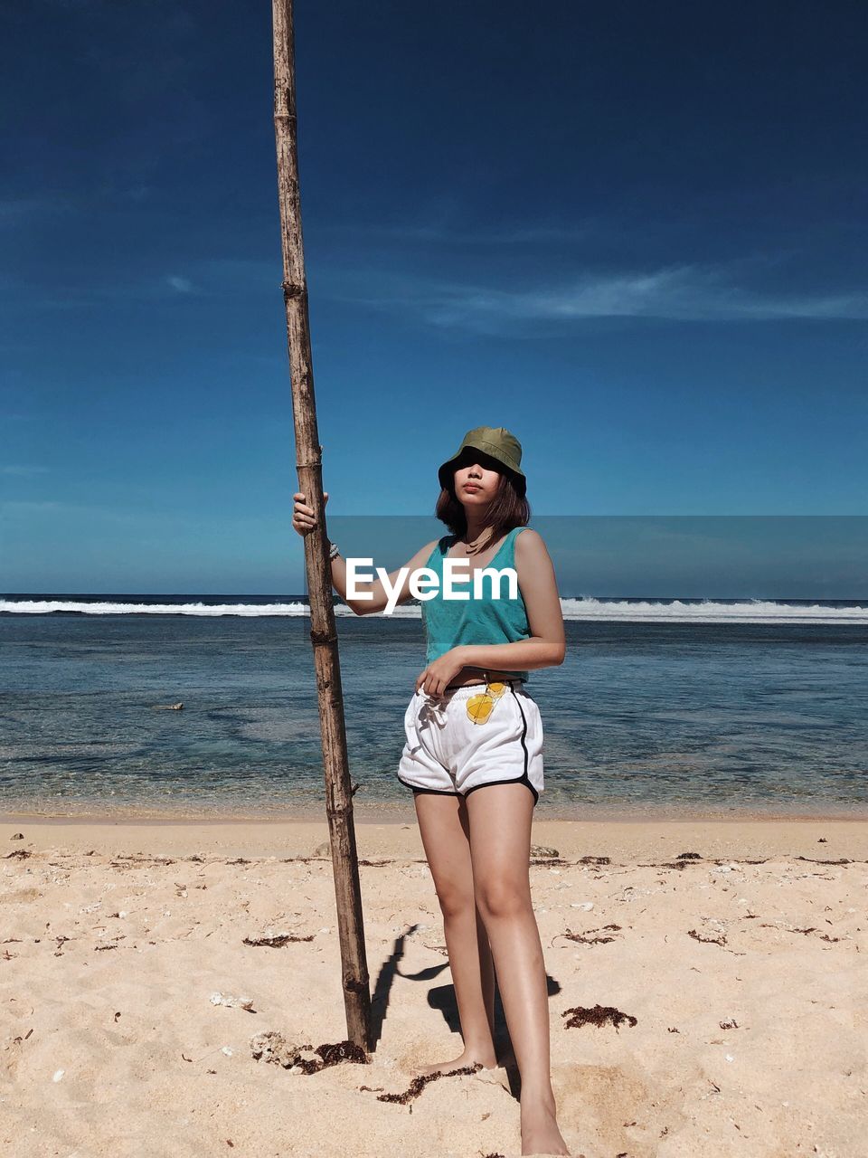 Full length of young woman standing at beach against sky during summer