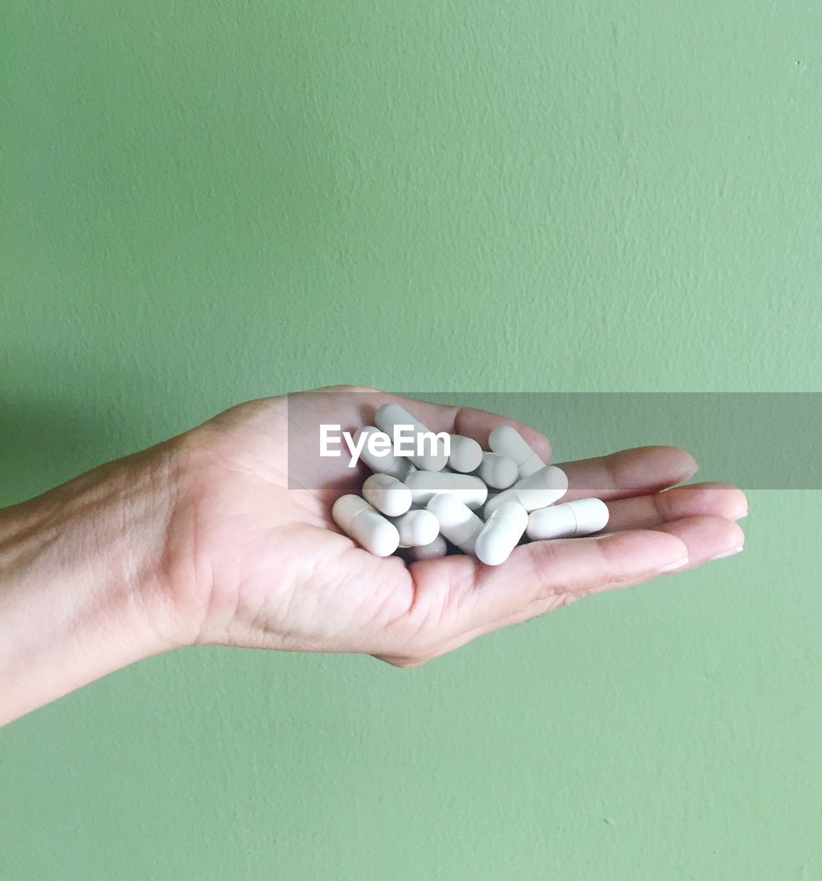 Cropped hand holding medicines against green wall