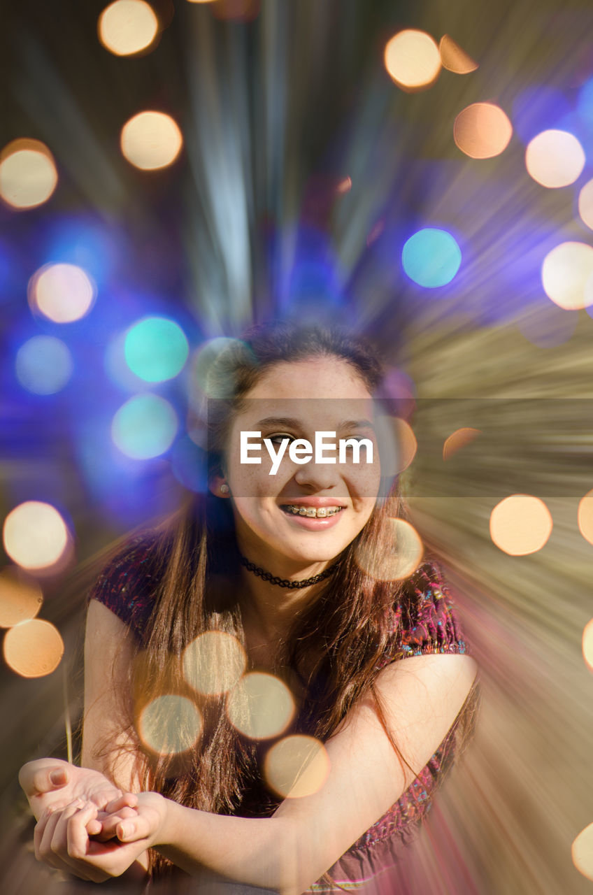 PORTRAIT OF SMILING YOUNG WOMAN IN ILLUMINATED LIGHTS