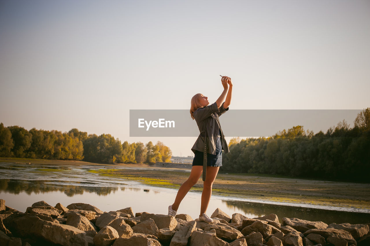 Woman photographing with mobile phone by lake