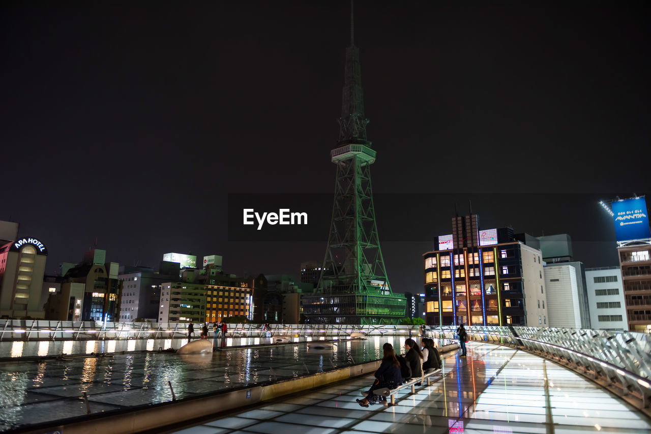 PEOPLE ON ILLUMINATED BRIDGE OVER RIVER BY BUILDINGS IN CITY