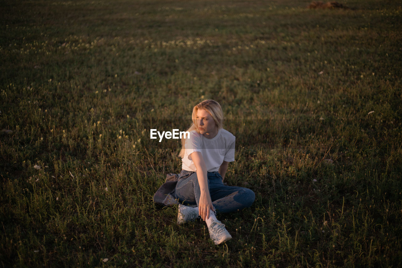 A young woman sitting in a field during sunset