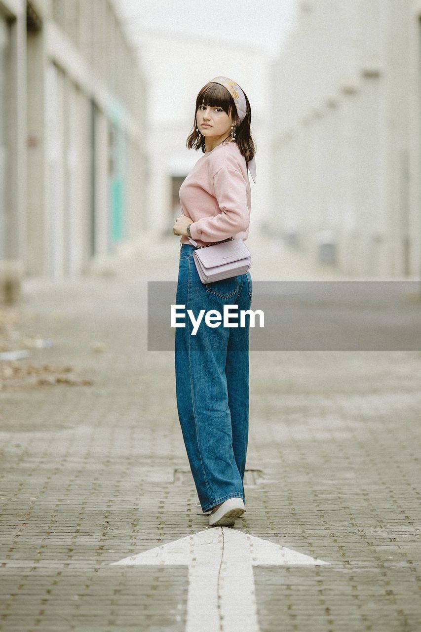 Portrait of young woman standing on footpath