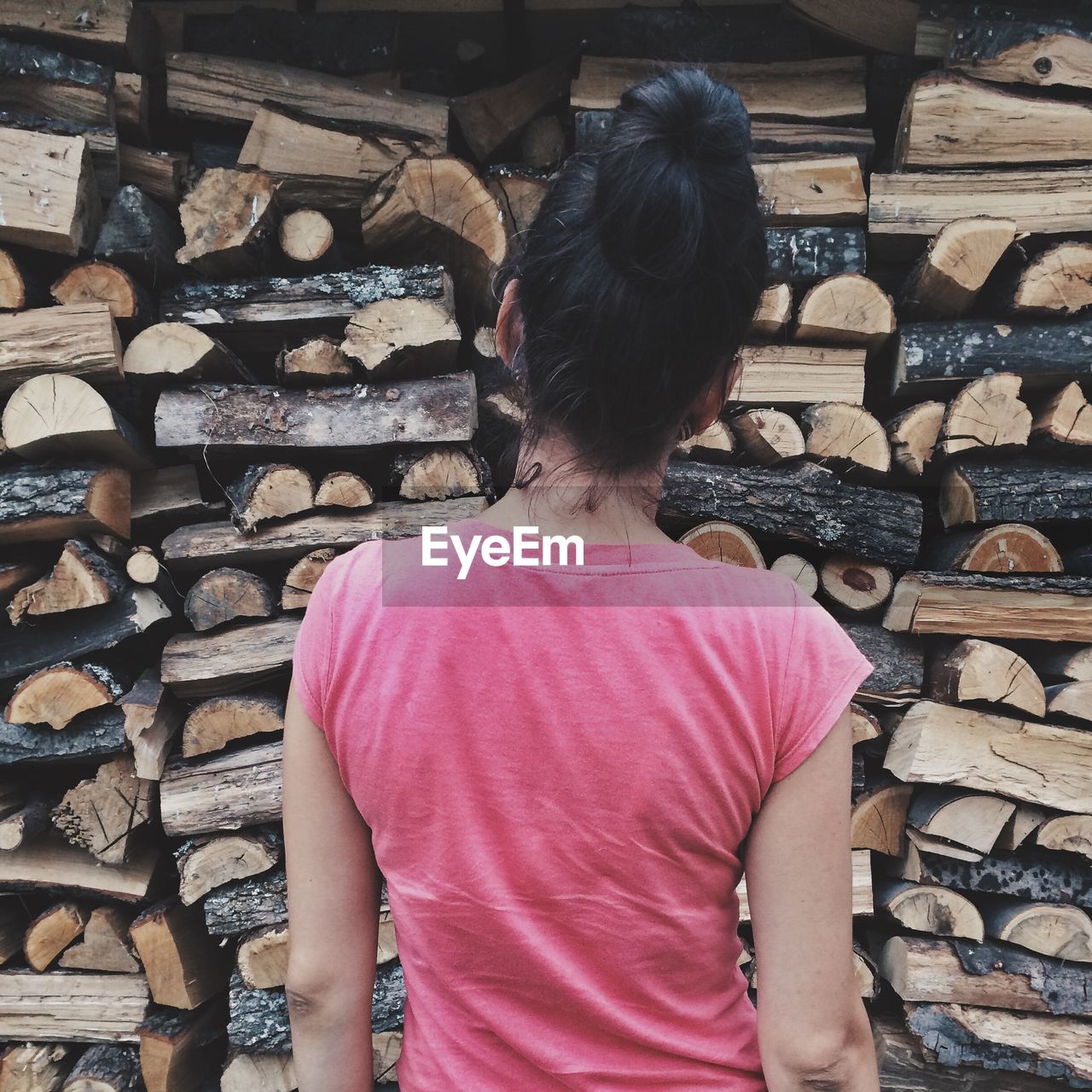 Rear view of woman standing against log stack