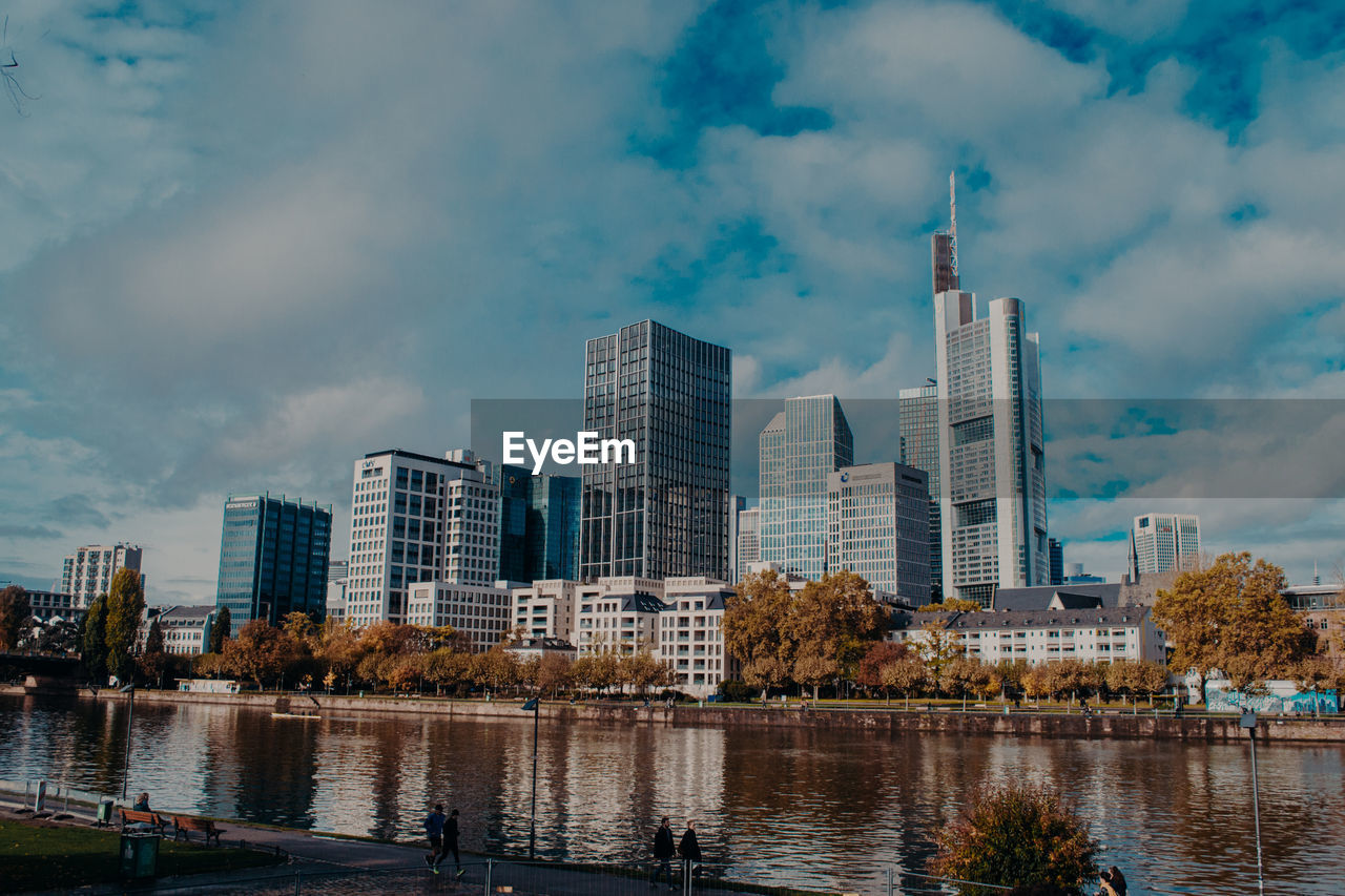 Modern buildings by river against sky in city