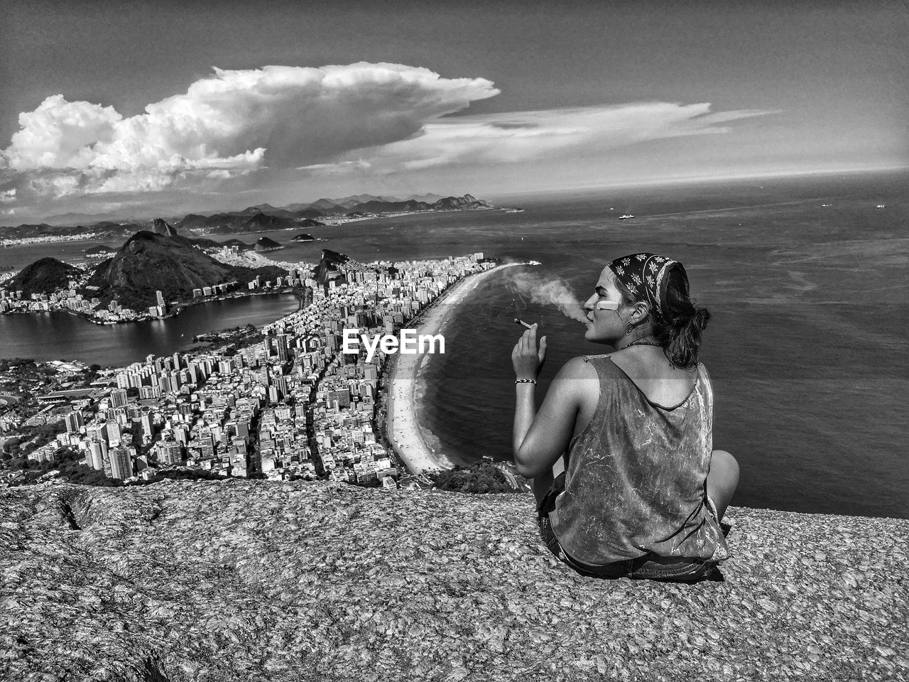 Young woman smoking cigarette while sitting over sea against sky