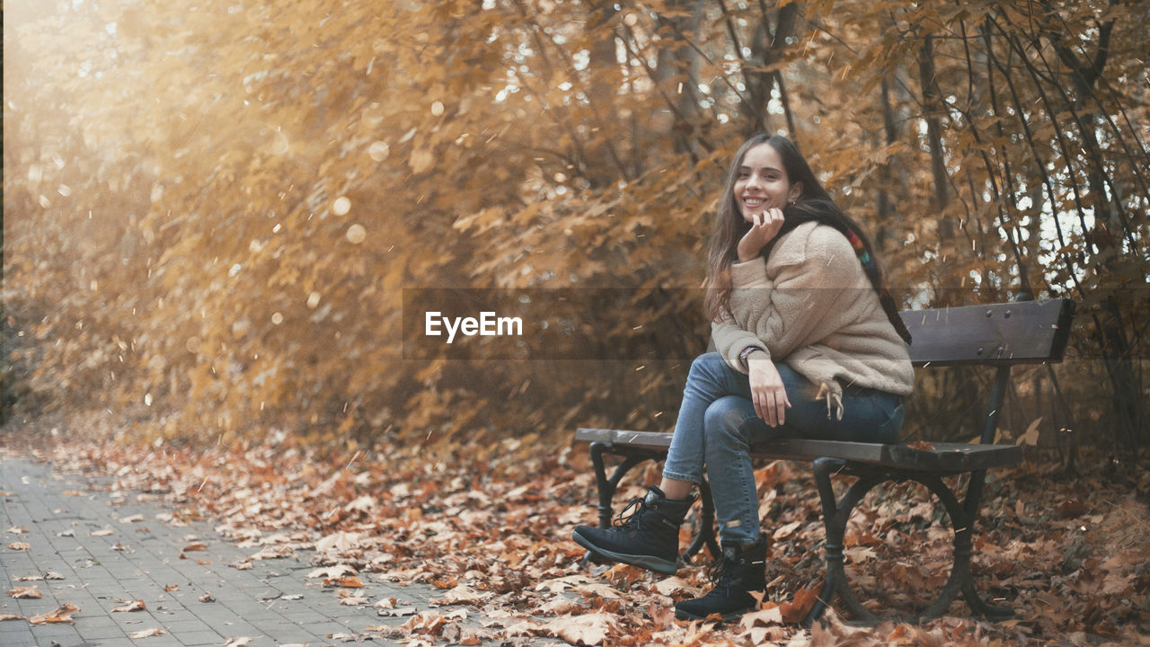 Young woman sitting on bench in park during autumn