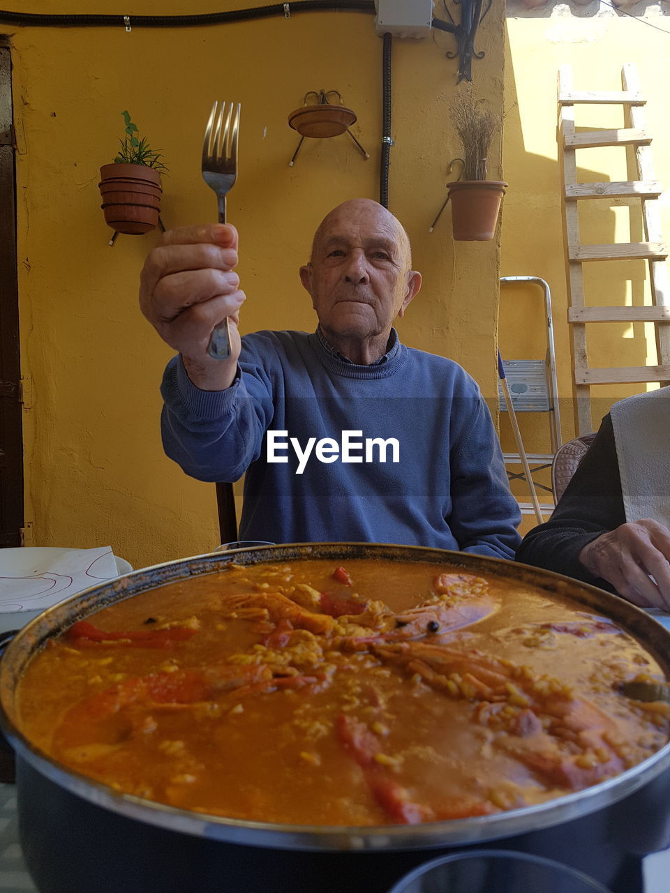 Senior man holding fork while sitting with food at table