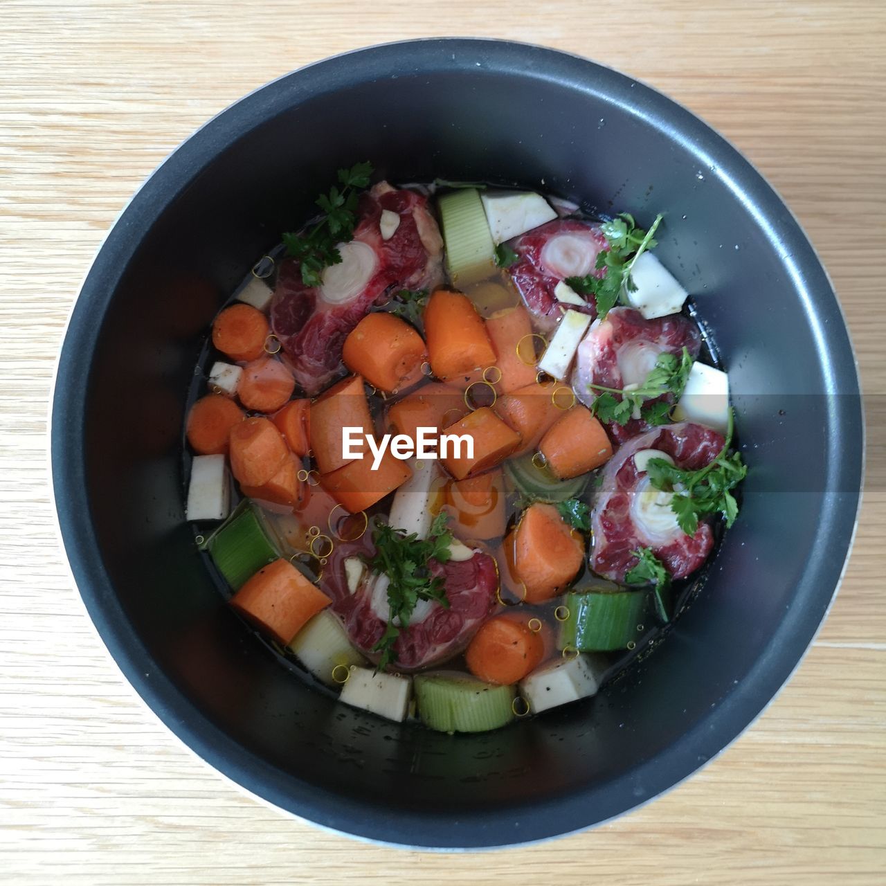 High angle view of chopped vegetables and oxtail in slow cooker bowl on table