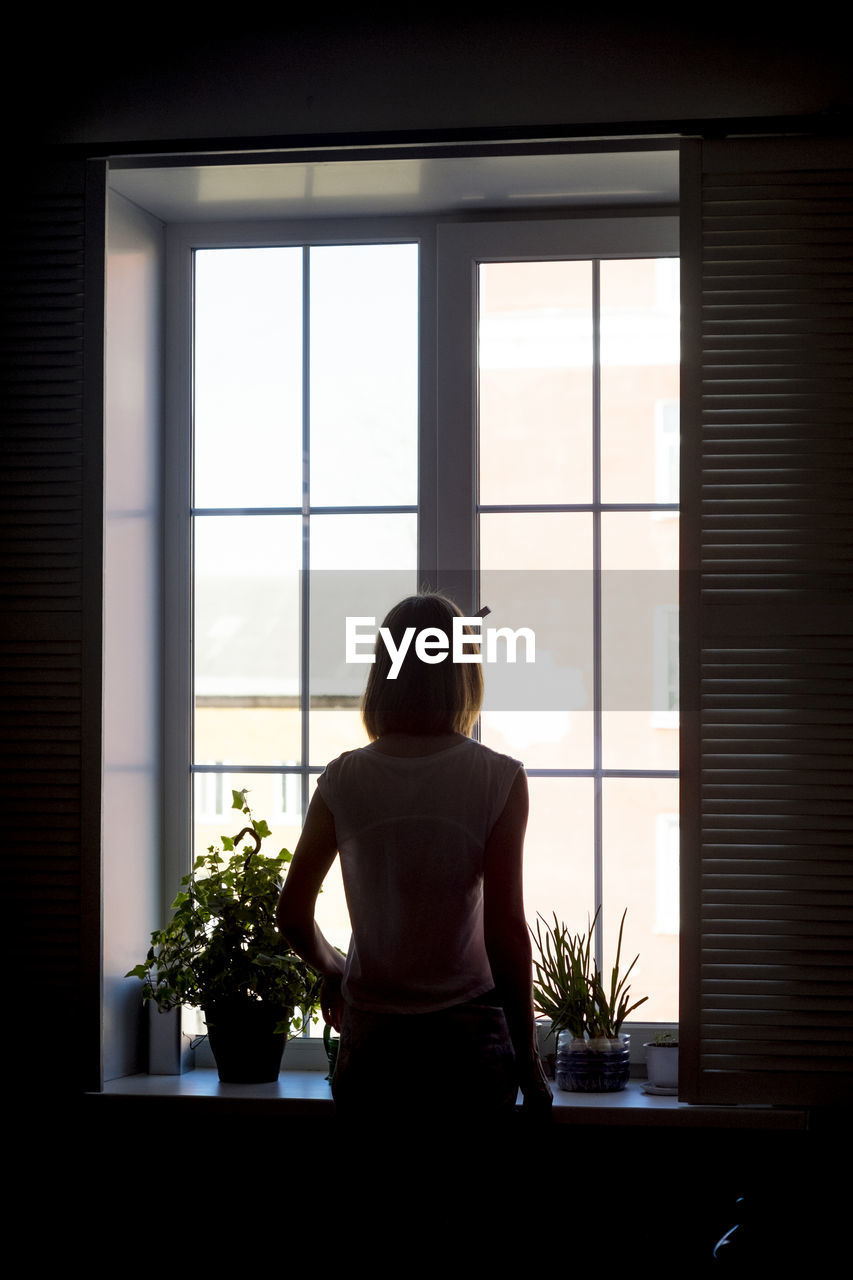 Rear view of woman standing by window