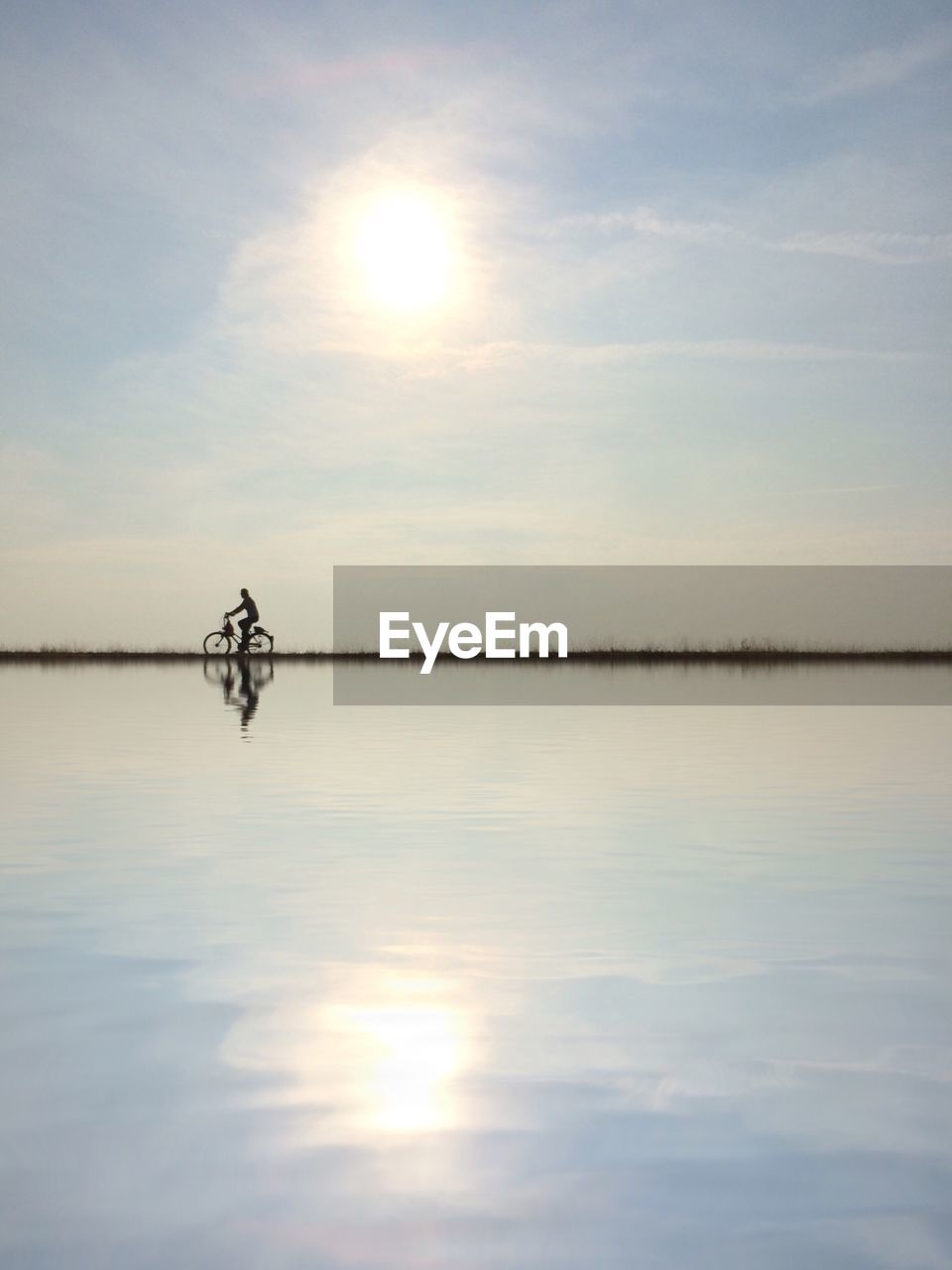 Reflection of man riding bicycle by lake at sunset