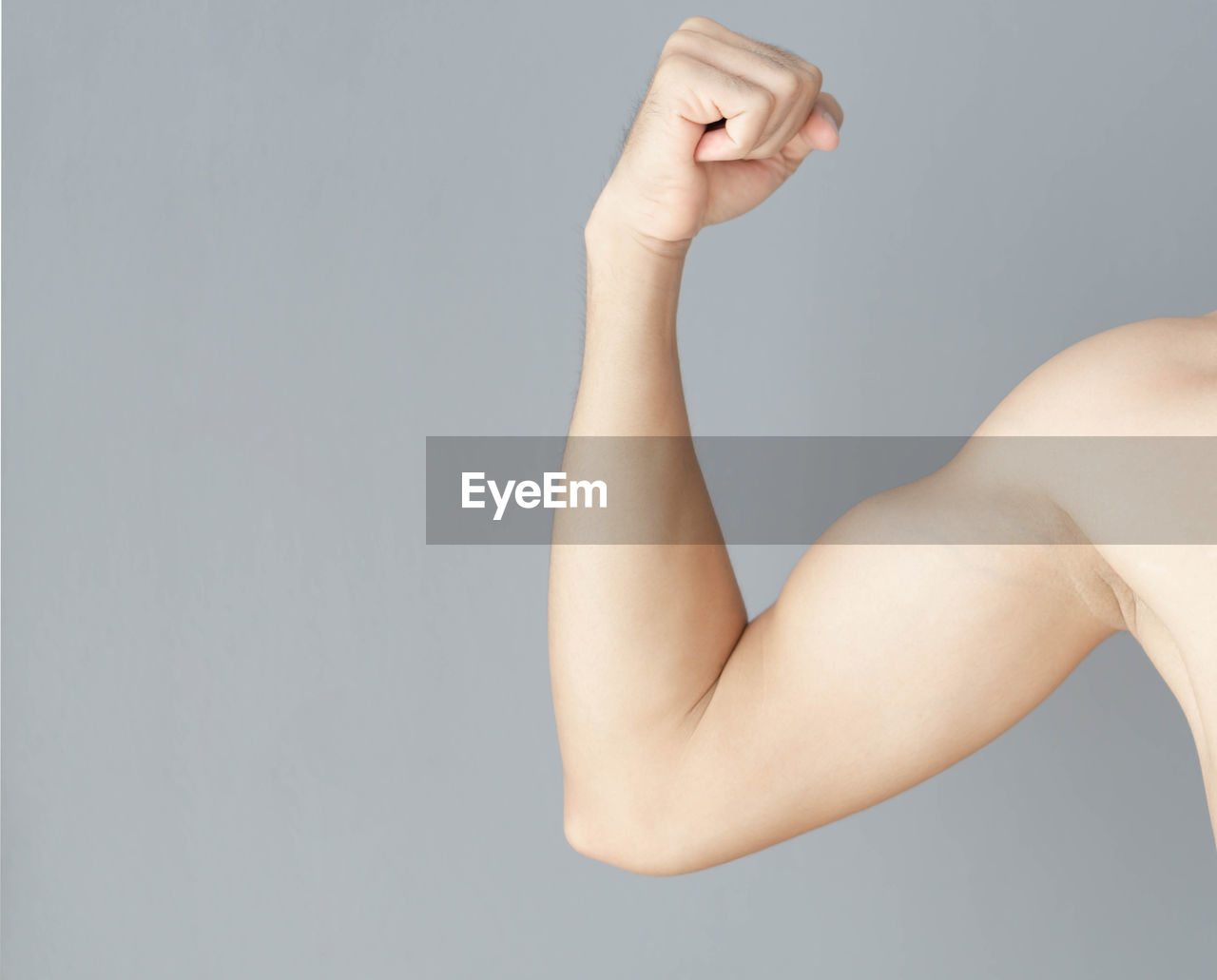 Cropped hand of man flexing muscles over gray background