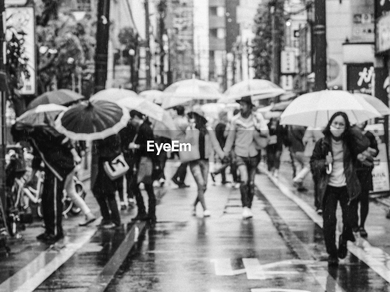 People holding umbrellas while walking on street during rainy season