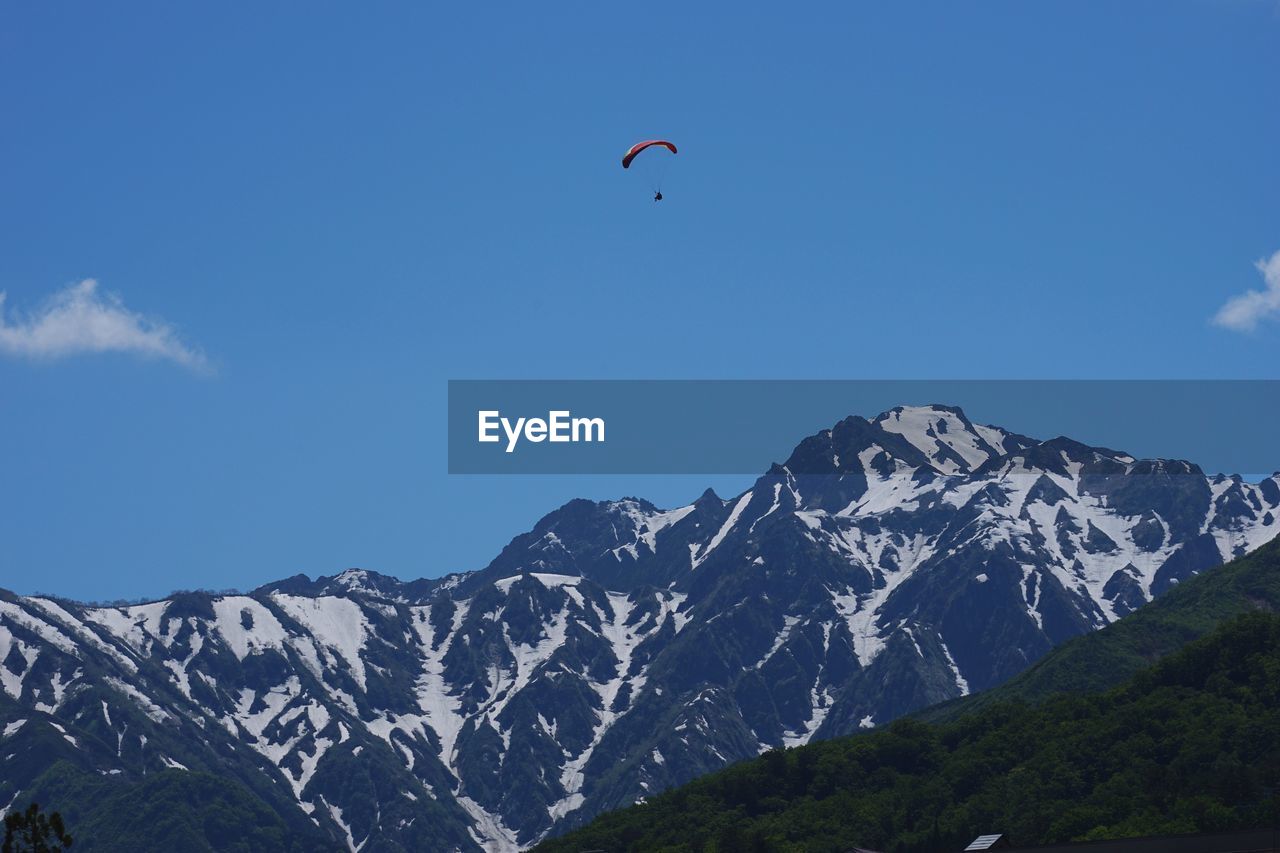 Person paragliding over snowcapped mountain against sky