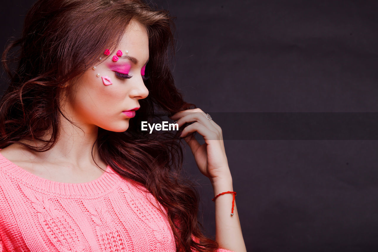 Close-up of beautiful young woman with make-up against gray background