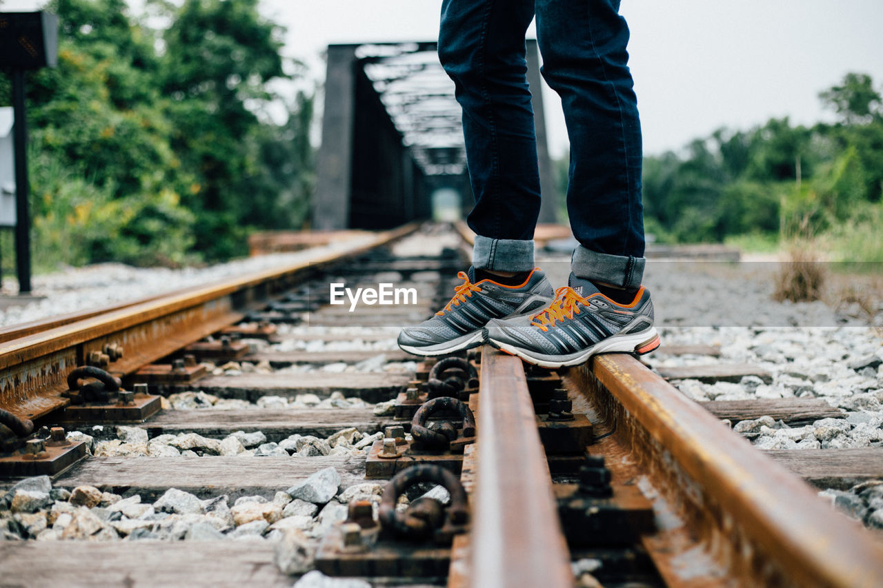 REAR VIEW OF WOMAN STANDING ON RAILROAD TRACKS