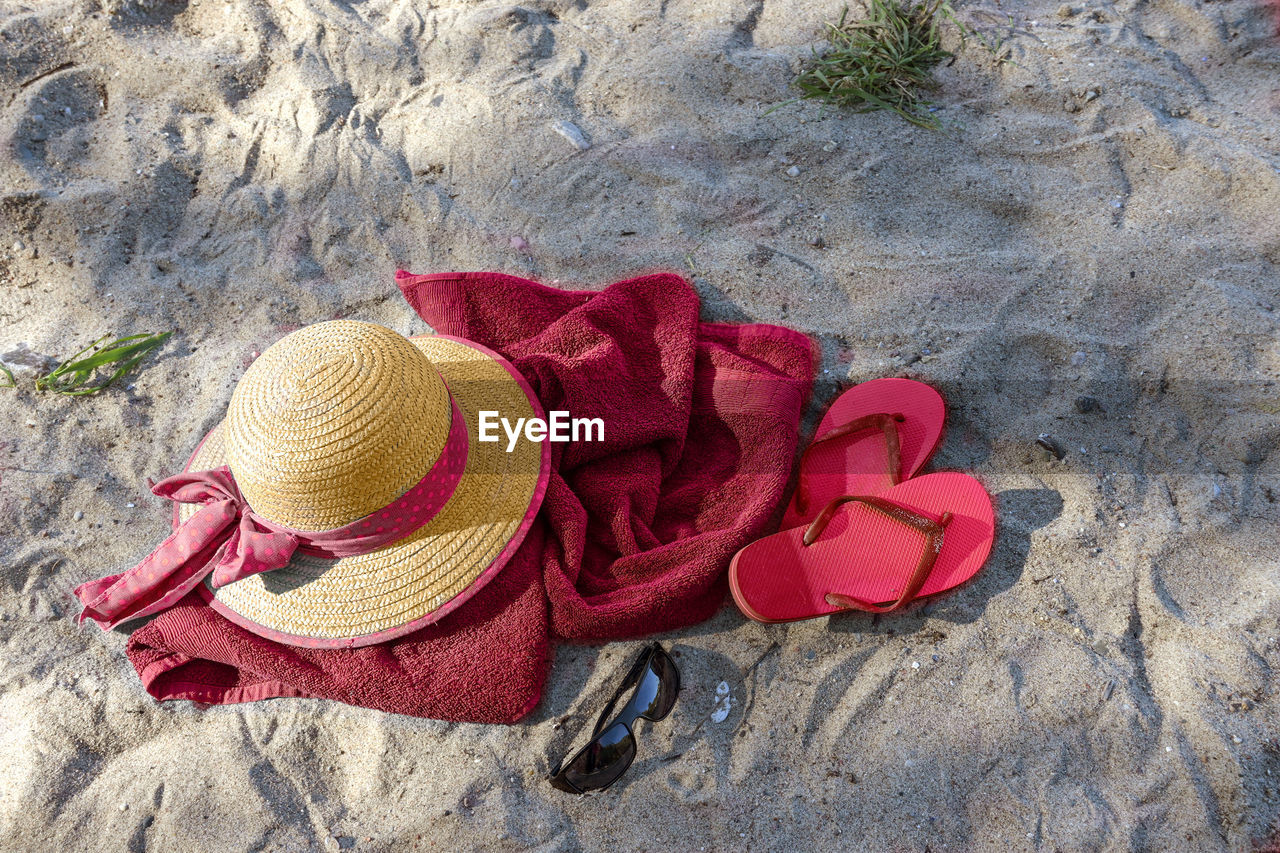 land, beach, red, hat, sand, high angle view, fashion accessory, sun hat, day, clothing, nature, no people, shoe, outdoors, flower, straw hat, sunlight, holiday, cowboy hat, pink, personal accessory, beauty in nature, pair, still life, vacation, trip, sandal