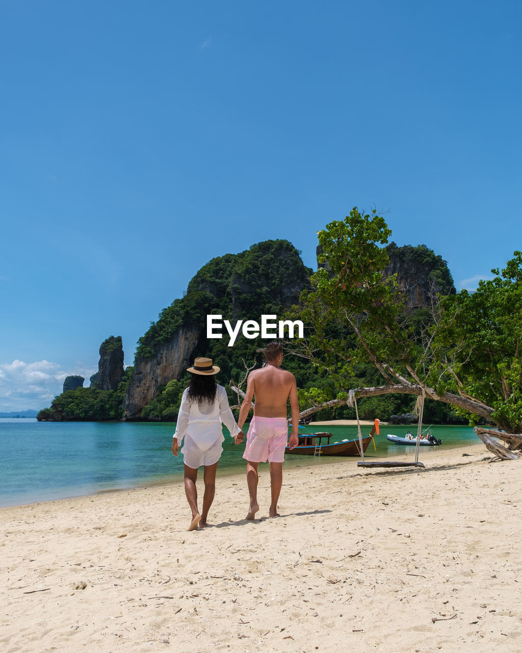 rear view of woman walking on beach against clear blue sky