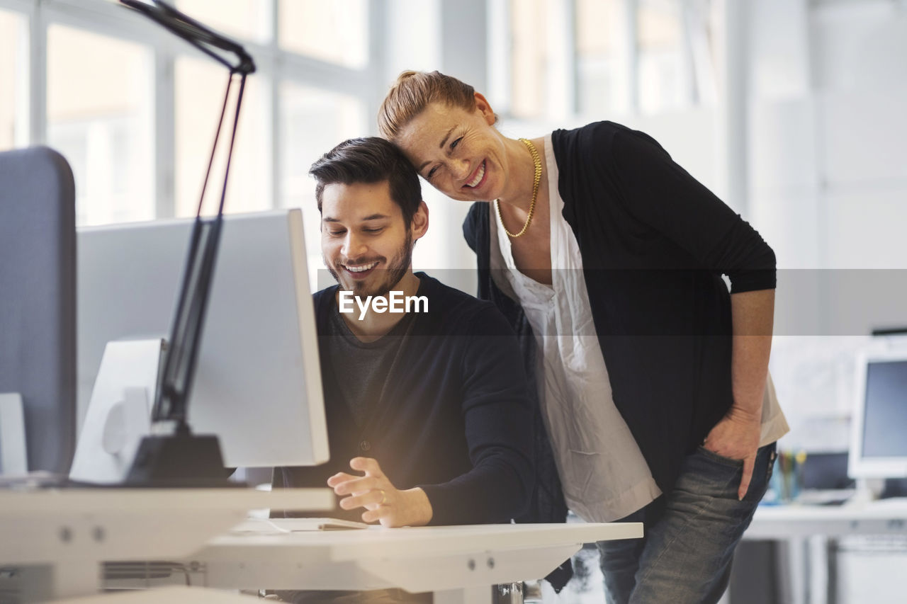 Happy businesswoman with male colleague using computer in office