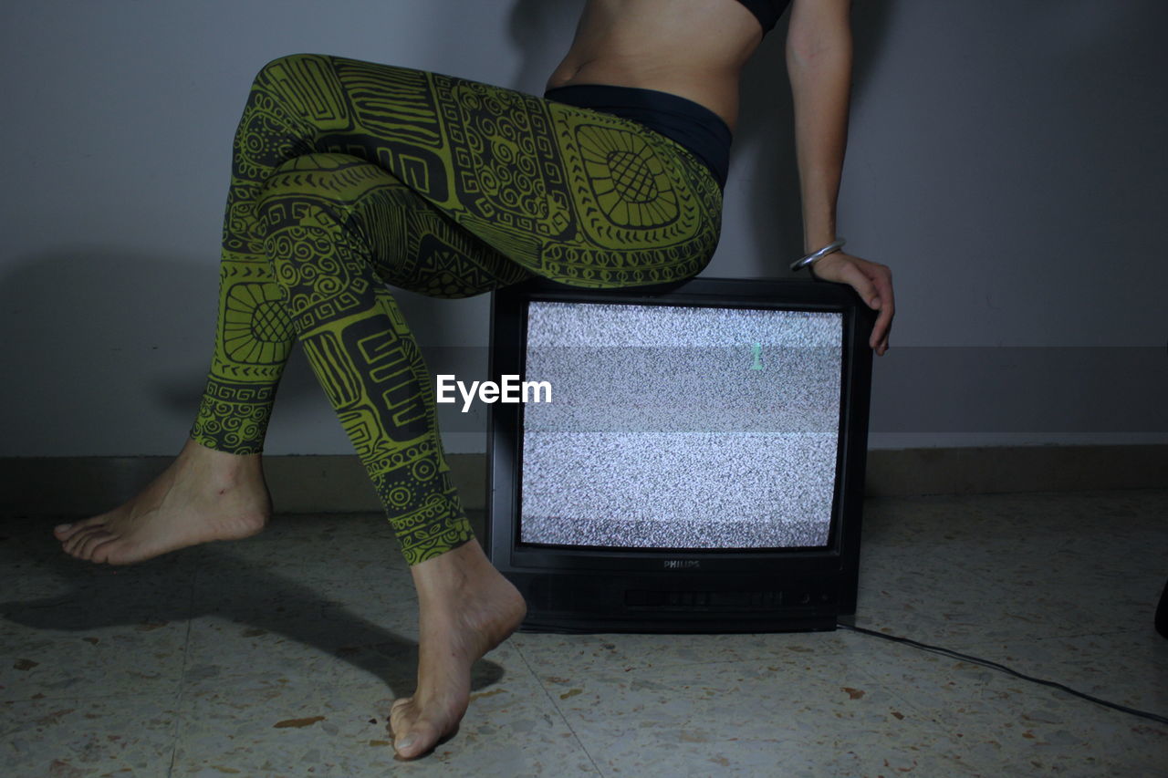 Low section of woman sitting on television set at home