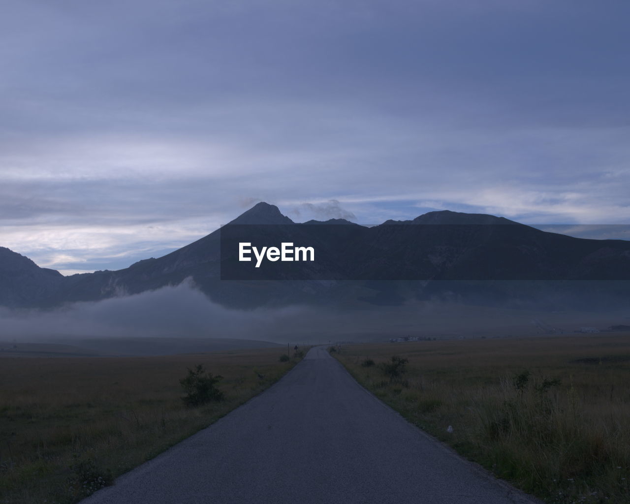 Empty road amidst field against mountains