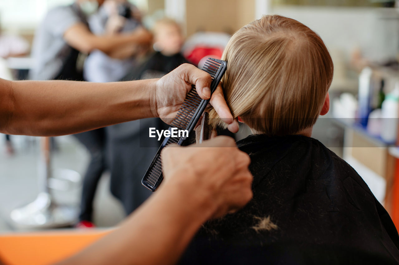 Crop barber doing haircut to little boy