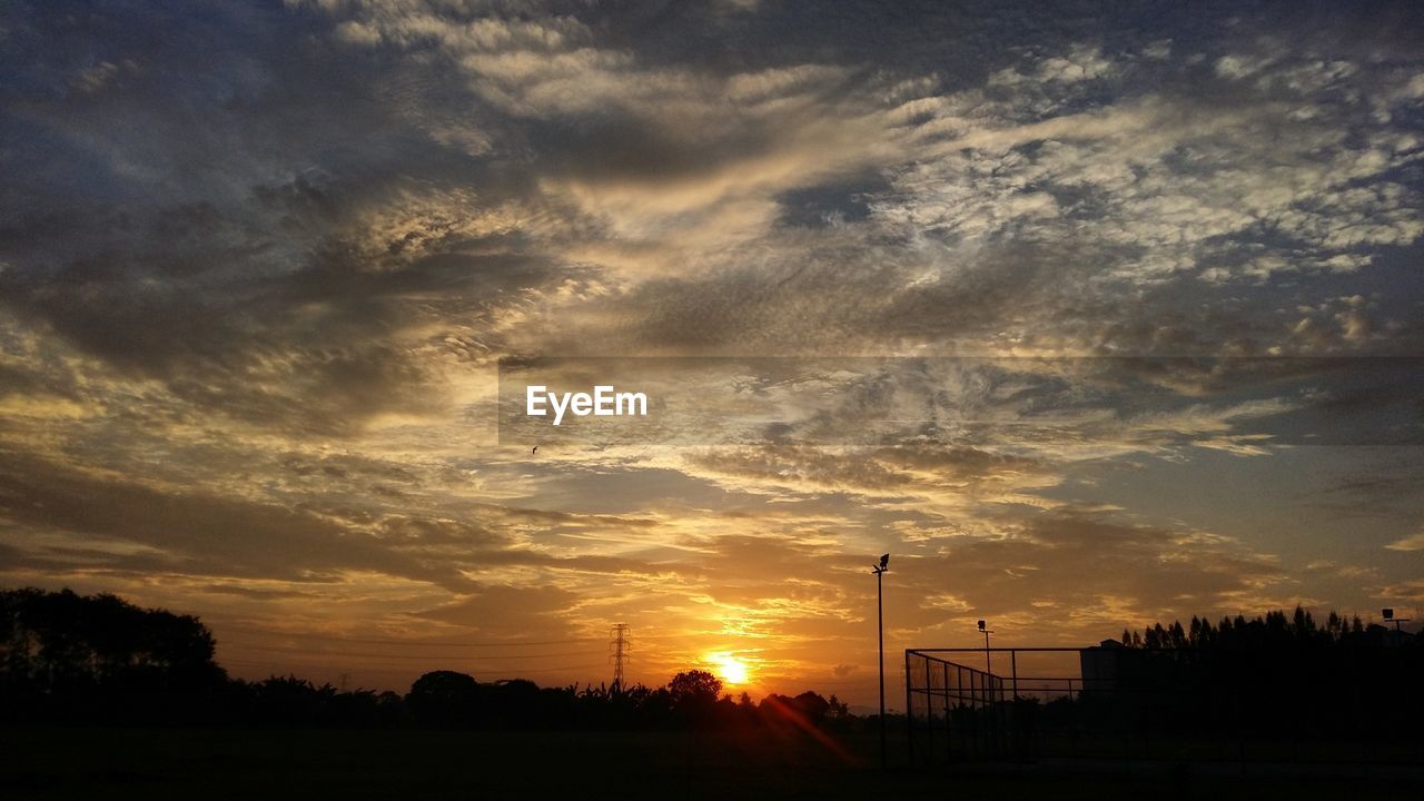 Silhouette trees on field against dramatic sky