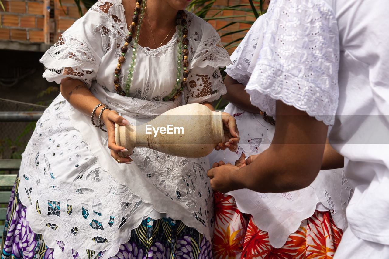 Midsection of person pouring water with vase on another person.