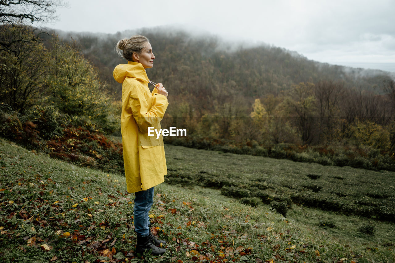 Middle aged woman in yellow raincoat walking in rainy weather in the countryside