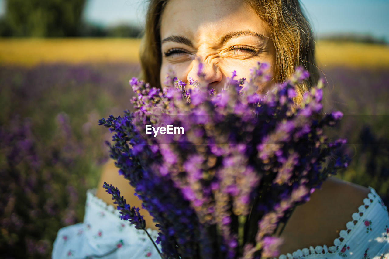 Close-up happy woman face with purple lavender flowers in summer field.