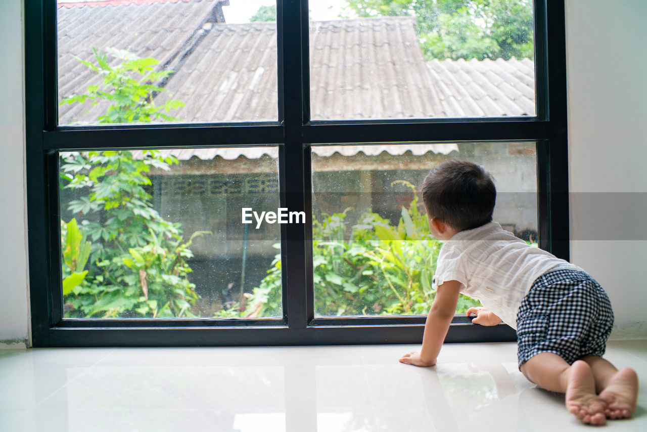 Full length of cute boy crouching by window at home