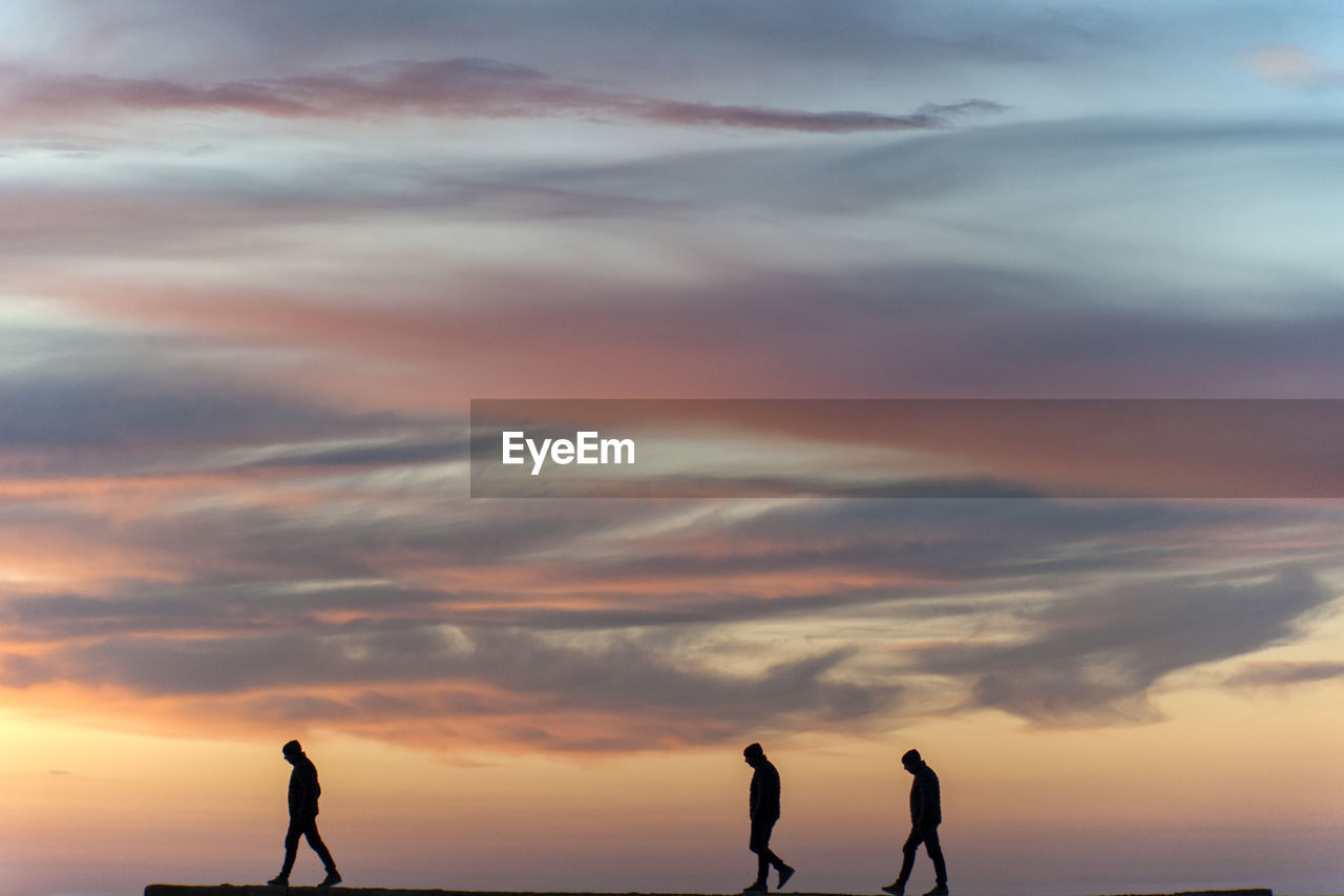 Silhouette people walking against sky during sunset