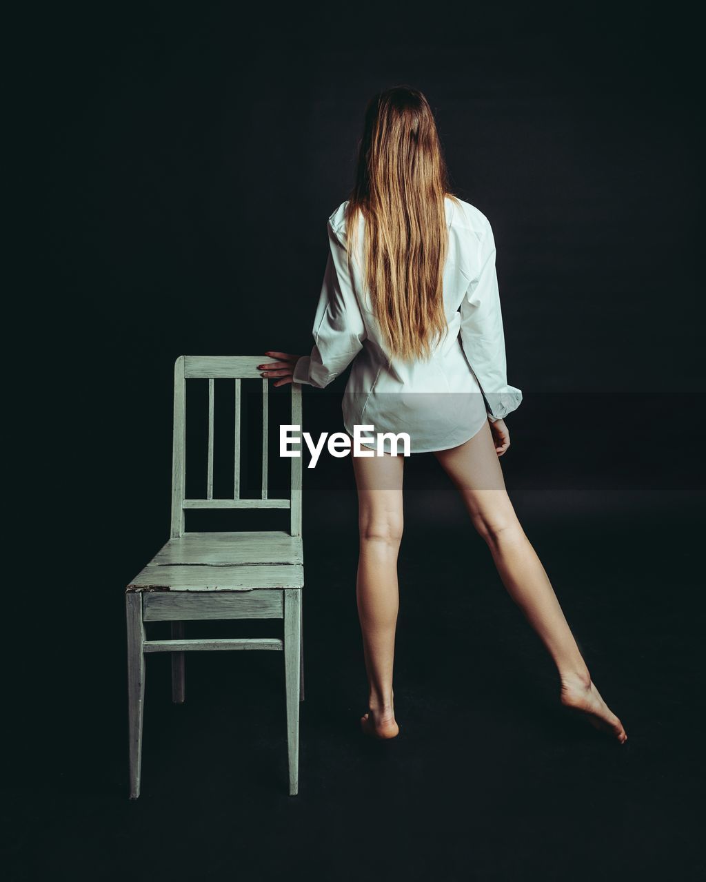 Rear view of woman standing by chair against black background