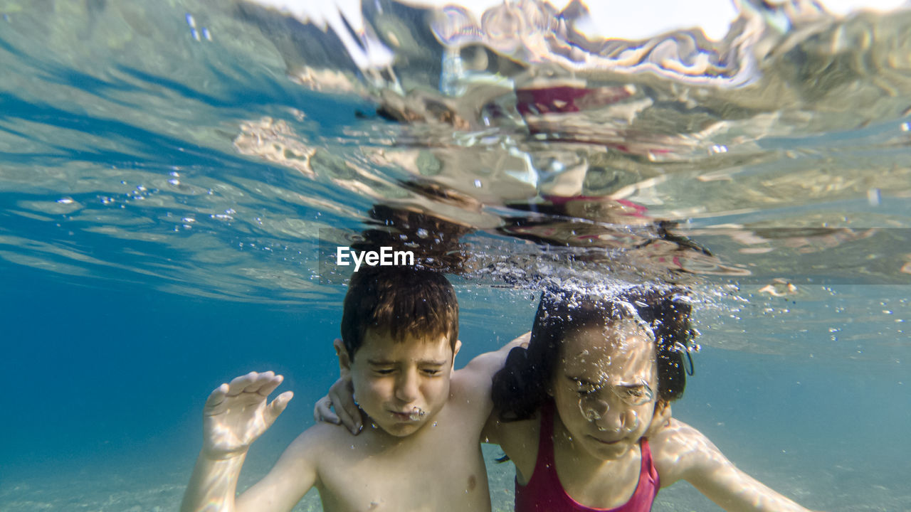 Siblings swimming underwater in pool