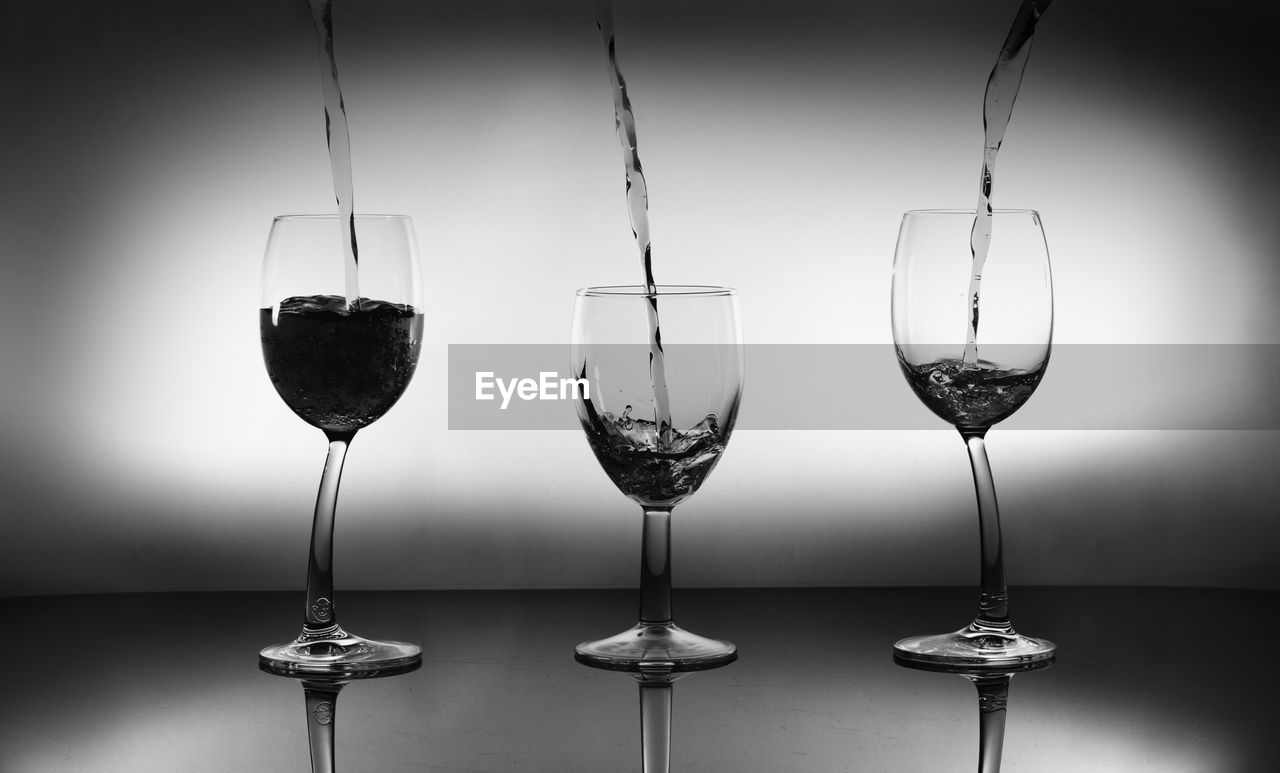 CLOSE-UP OF WINE GLASSES ON TABLE AGAINST GLASS BACKGROUND