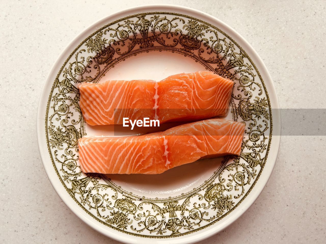 Overhead shot - 2 fresh salmon fillets. pinky orange fish. in ornate green and white plate.