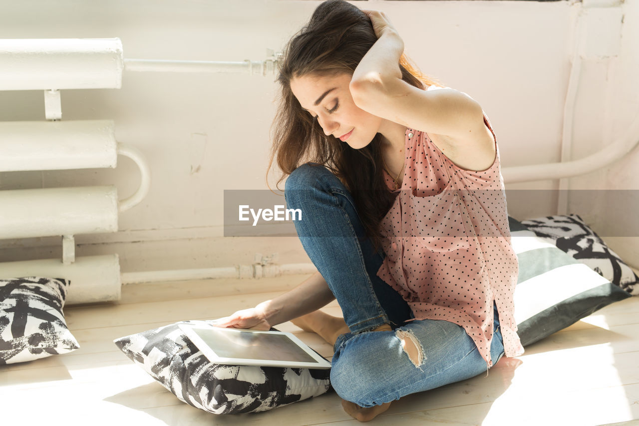 YOUNG WOMAN USING MOBILE PHONE WHILE SITTING ON WALL