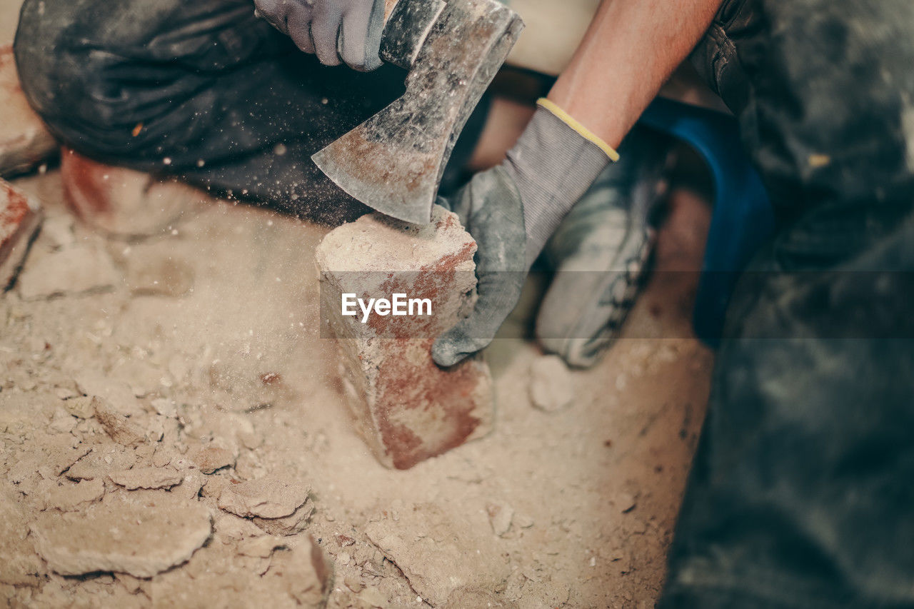 A young man cleans bricks with an axe.