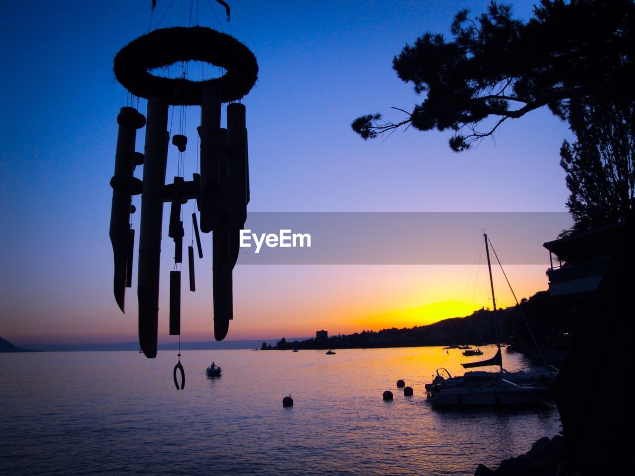 Silhouette wind chime hanging by lake against sky during sunset