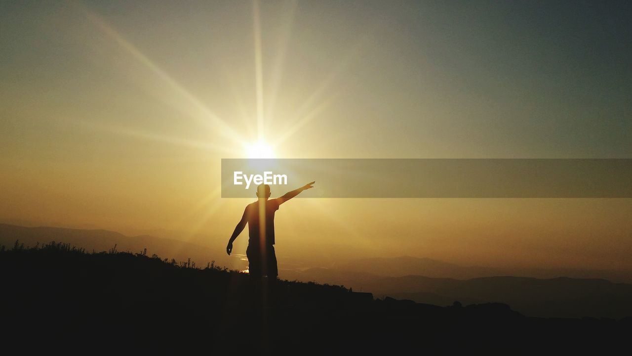 Silhouette man with arms outstretched standing against sky during sunset