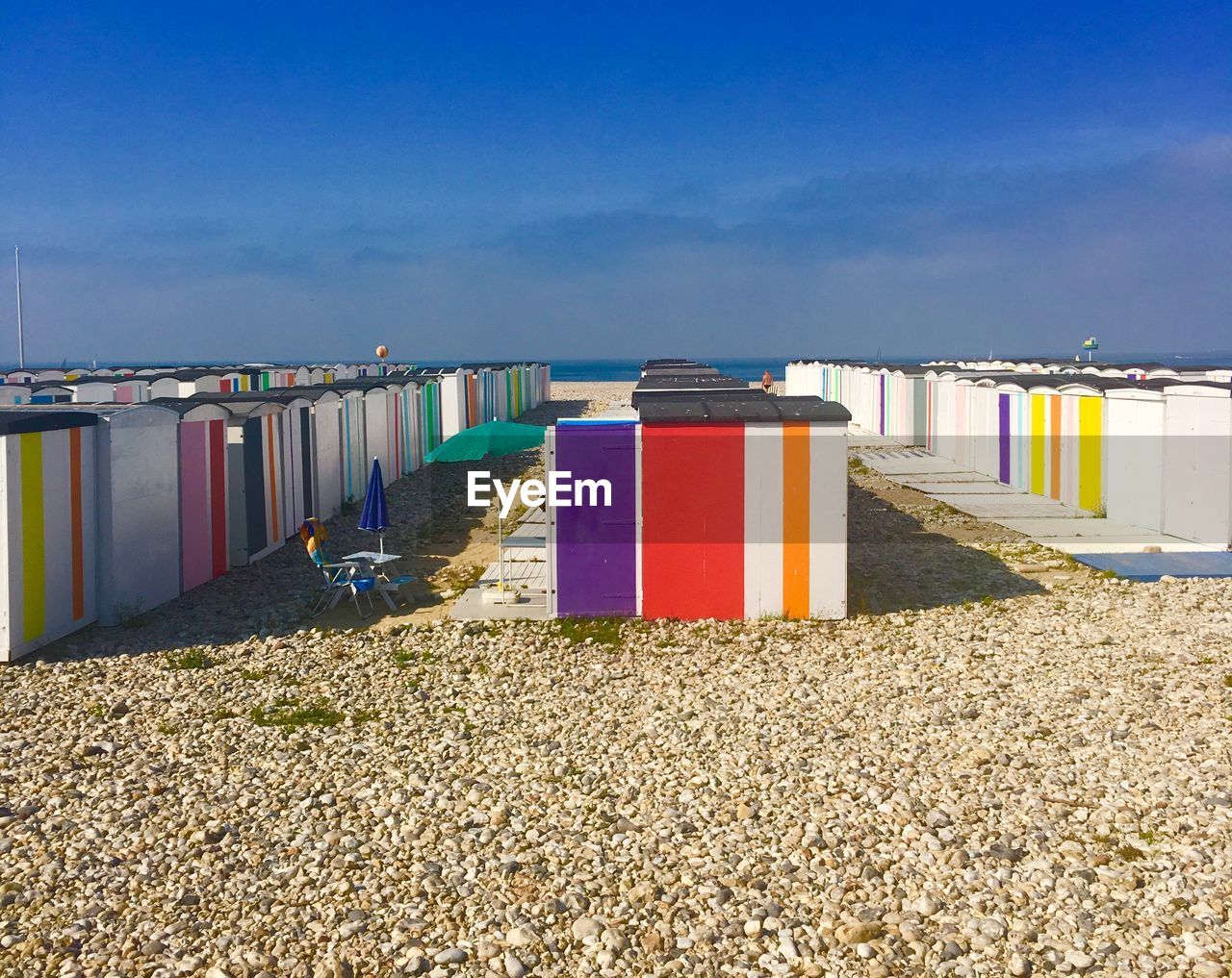 Row of hooded chairs on beach against blue sky