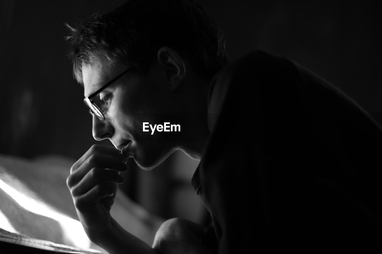 Side view of serious young man reading book in dark room