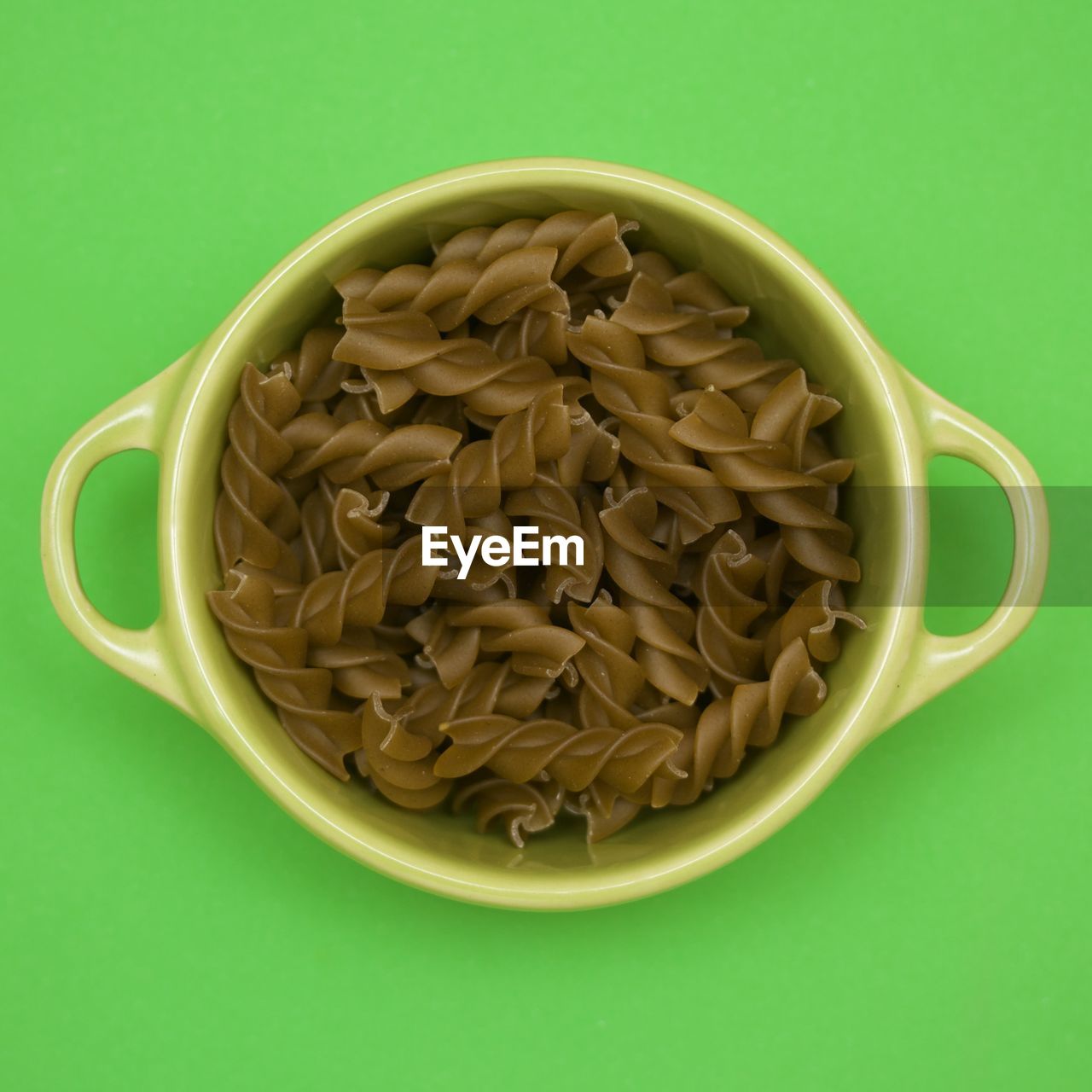 Green fusilli pasta in a green bowl on green background