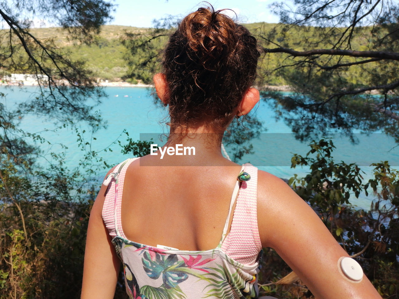 Girl with diabetes looks at the turquoise sea. on right arm is placed white sensor for  cgm devise.