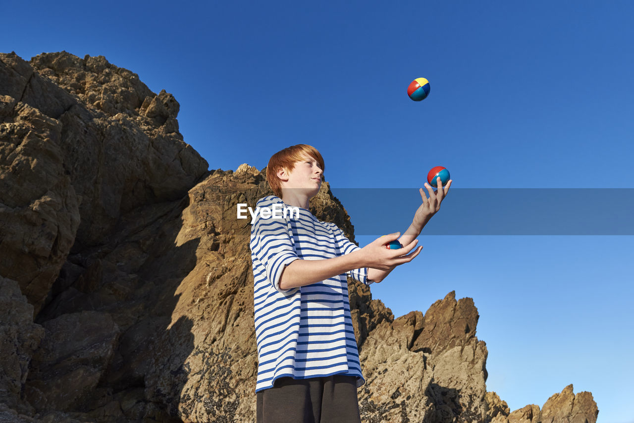 Boy juggling balls while playing against clear sky