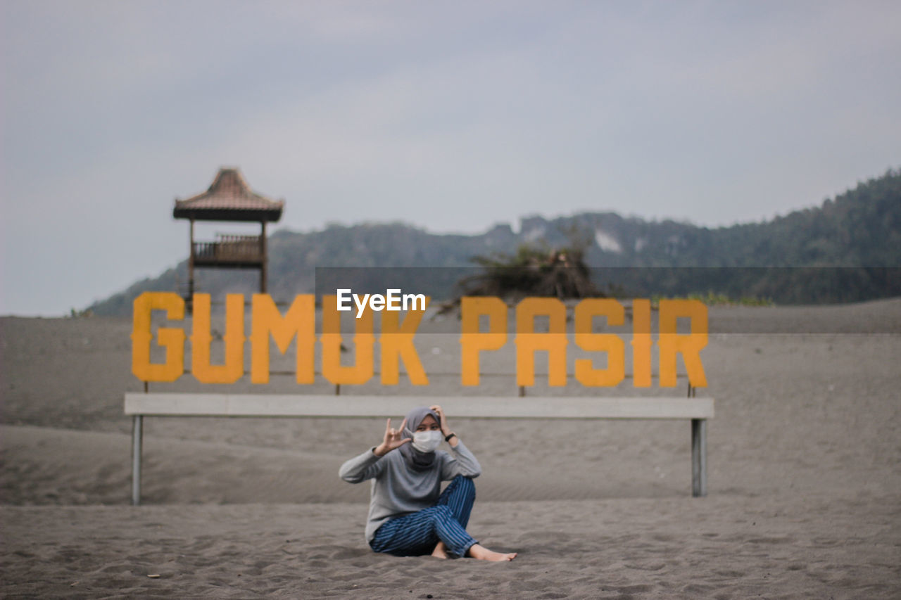 Full length of woman sitting on sand against advertisement