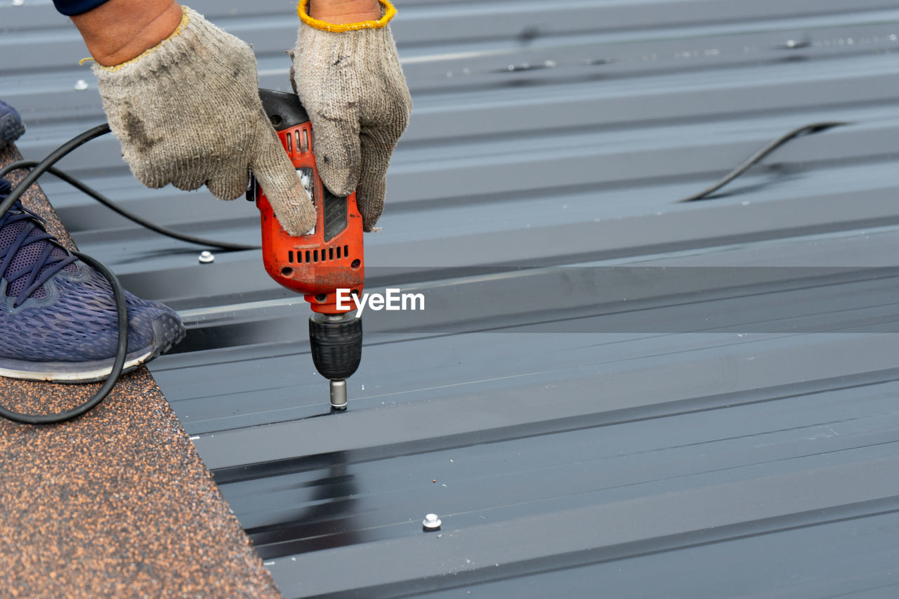 Workers installing the metal sheet roof by electrical drilling machine. 
