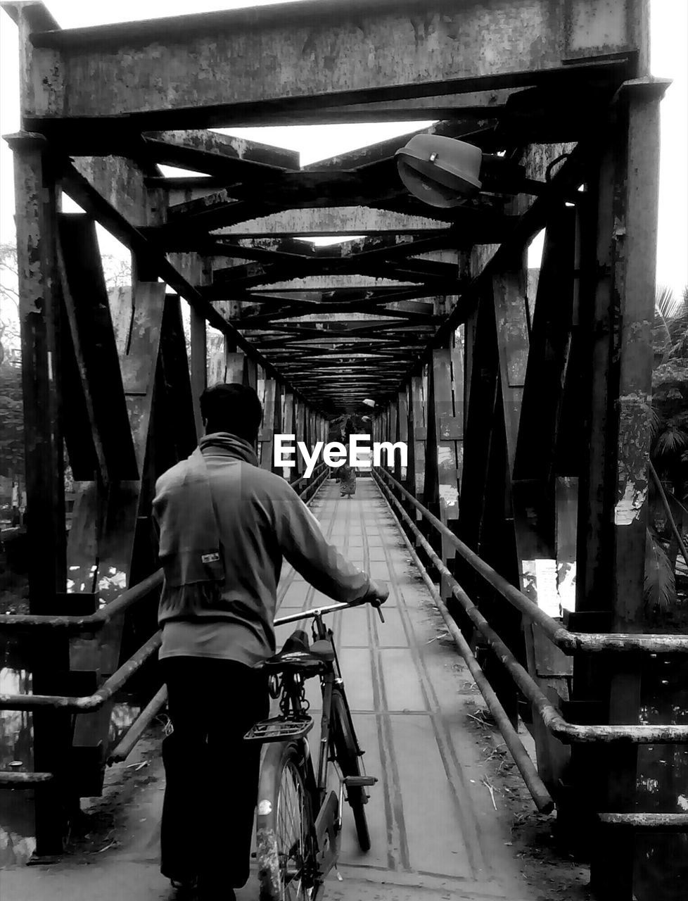 Rear view of man with bicycle walking on bridge