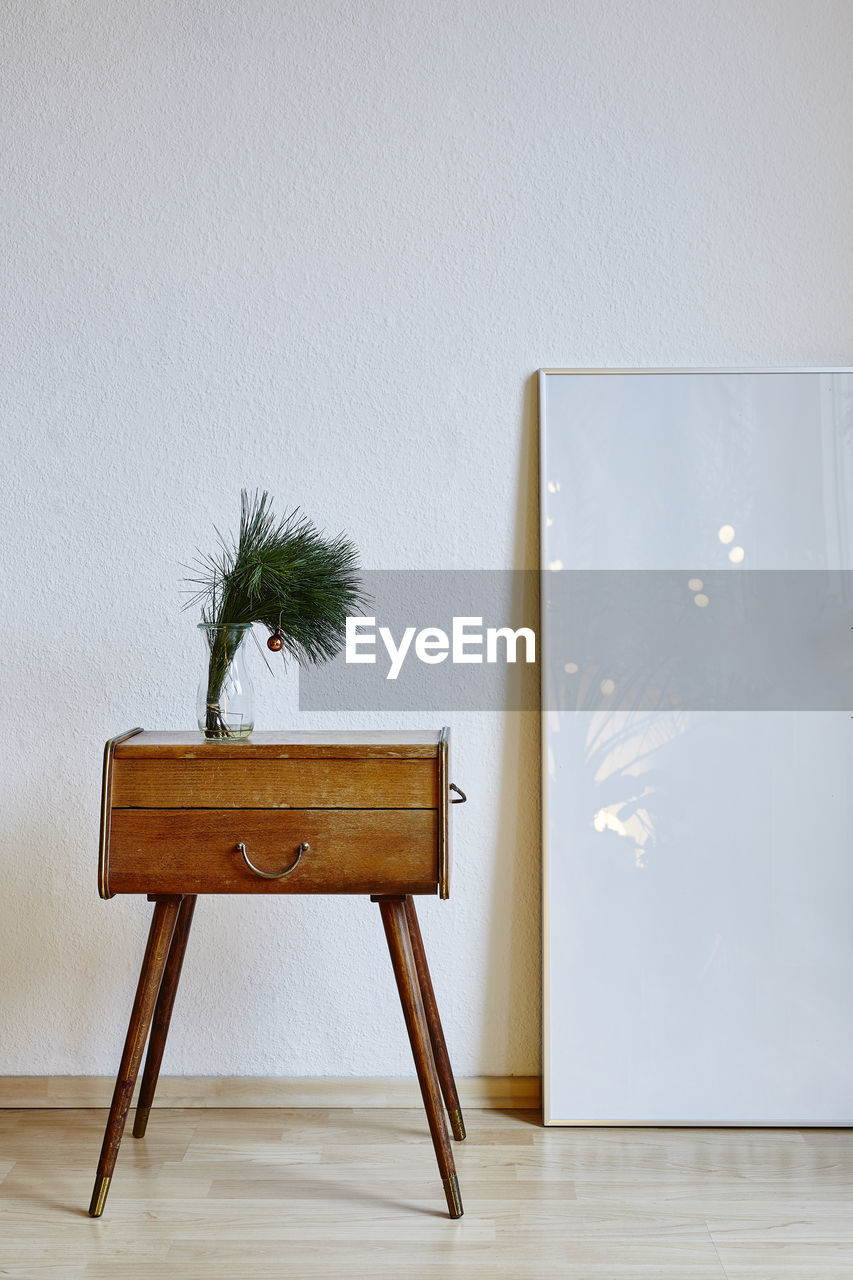 Potted plant on drawer with picture frame by wall